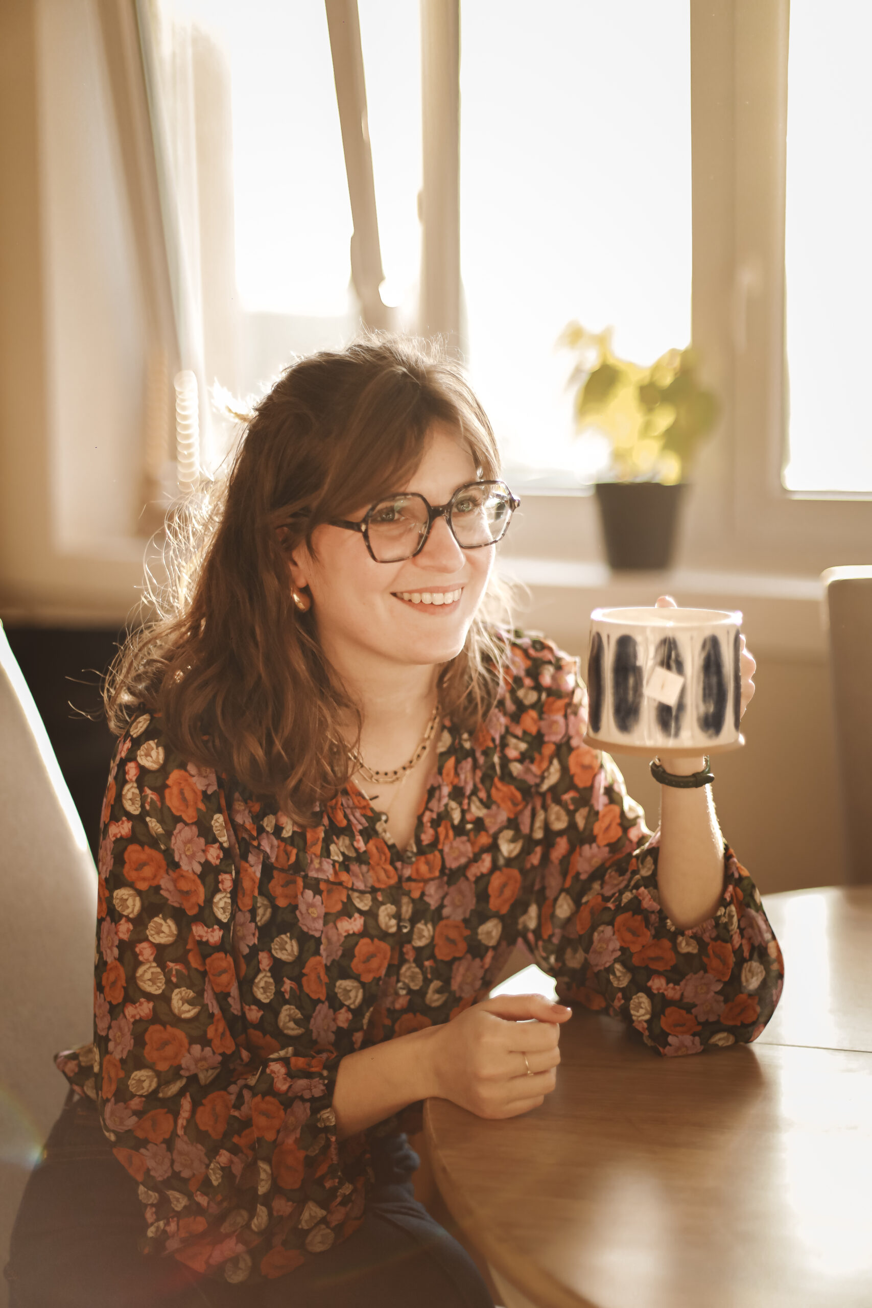 une femme assise à une table tient une tasse de thé