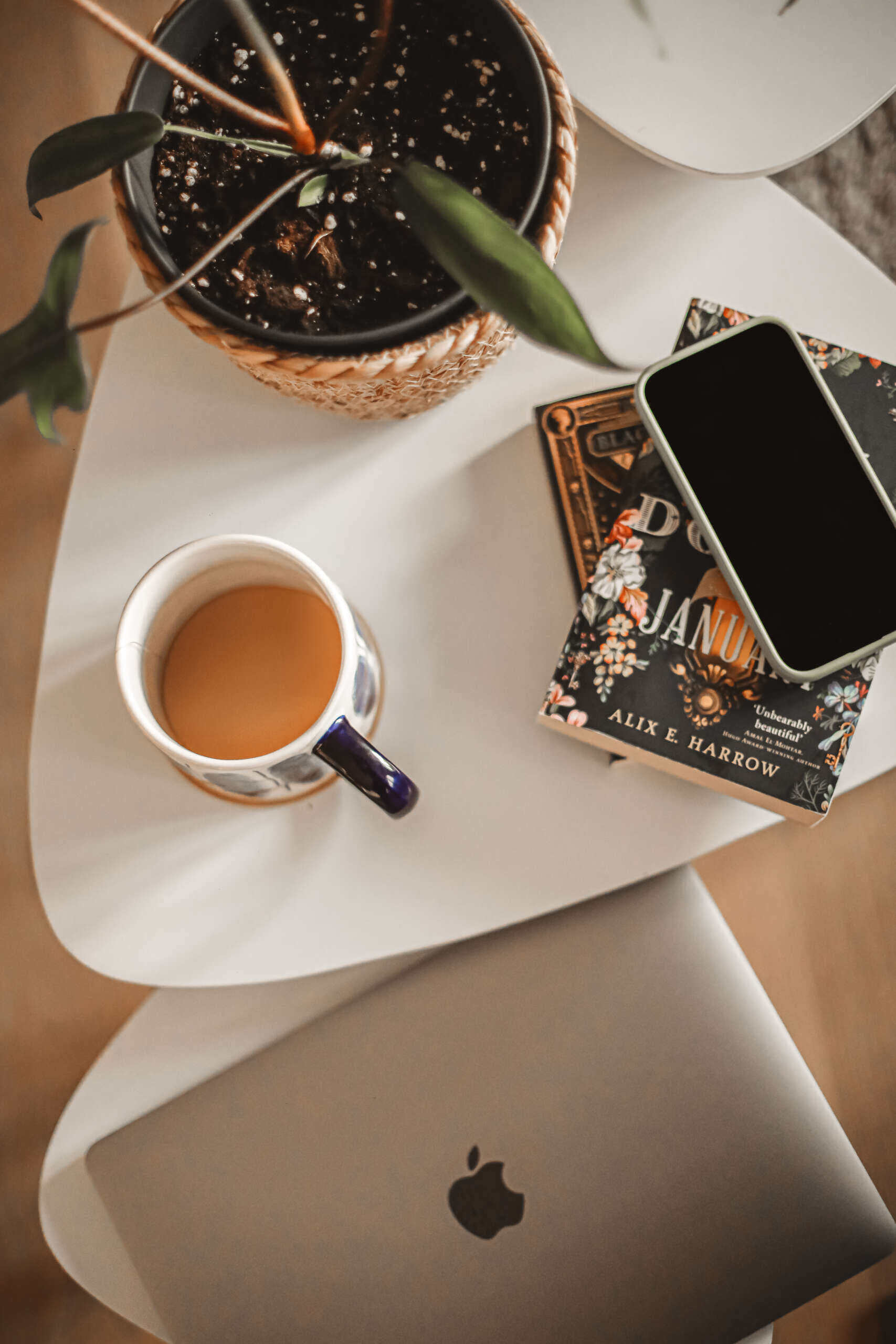 un ordinateur, des livres, une tasse de thé et une plante sur des tables gigognes
