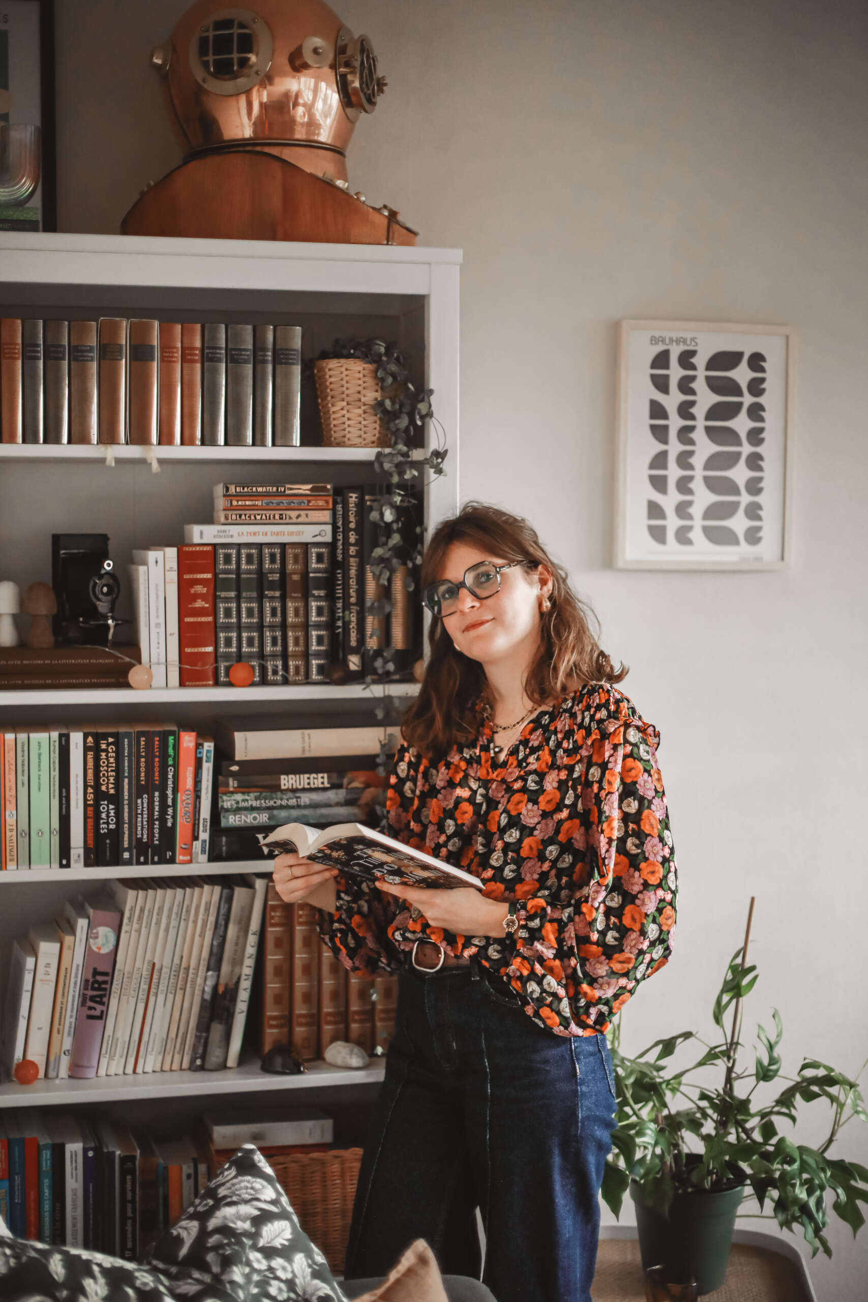 une femme adossée à une bibliothèque avec un livre dans ses mains